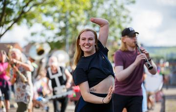 Musicians and dancers rehearse outdoors for SMOOSH! in late 2020. The subject of the photo is a dancer with long red hair and a limb difference, smiling as she strikes a pose.