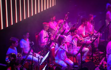 The woodwind section of Paraorchestra playing their instruments on stage illuminated in vivid pink light