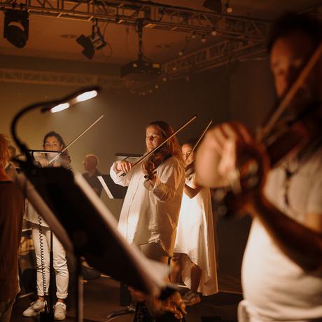 A trio of violinists illuminated in soft yellow light.