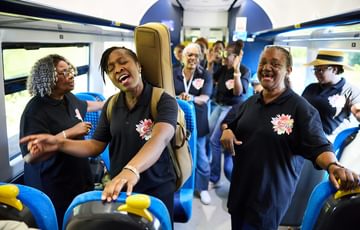Members of the Celebration gospel choir smile and clap as they perform on inside a train carriage.