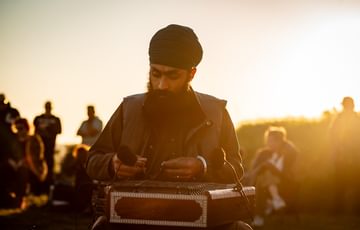 Eeshar Singh, a Sikh man in his late twenties wearing a round turban with a medium-length black beard. He is sitting cross-legged, looking down intently as he plays the santoor on his lap, a small string instrument played with two small wooden hammers.