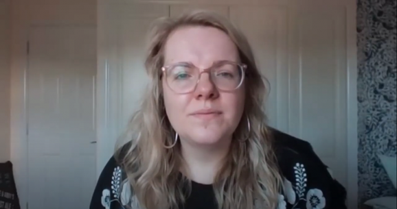 Kate McStraw, a person with light skin and long blonde hair, wearing glasses, hoop earrings and a black top is speaking to the camera on Zoom.