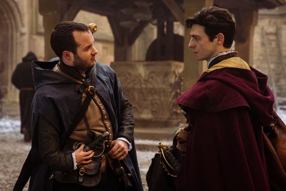 A still image from the Shardlake TV series. Two men in Tudor period dress converse in a church.